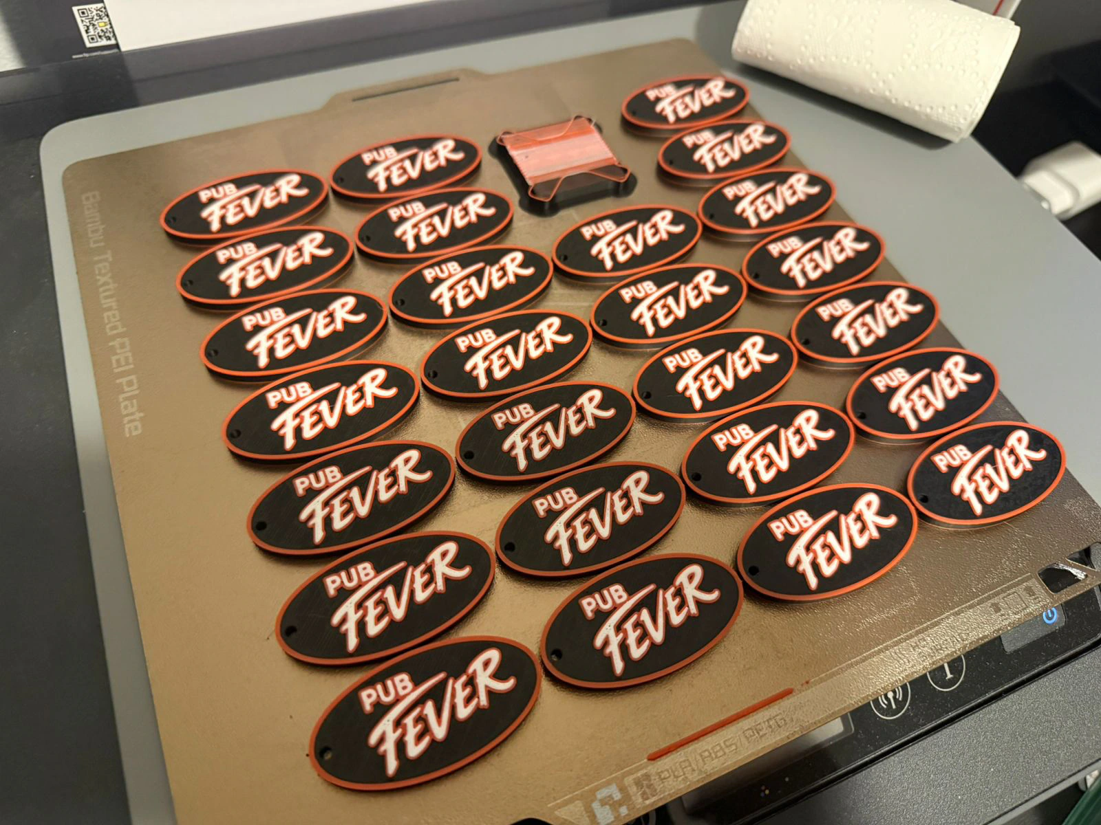 A full printing plate of black Pub Fever keychains with red borders and white lettering.