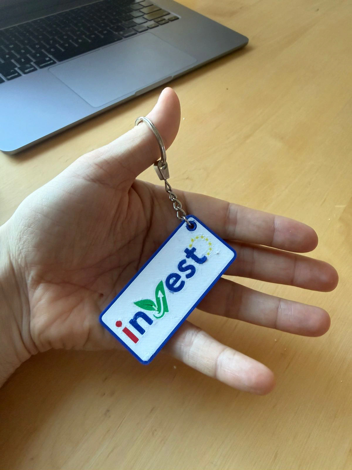 A rectangular blue-and-white inVest logo keychain held in a person's hand.
