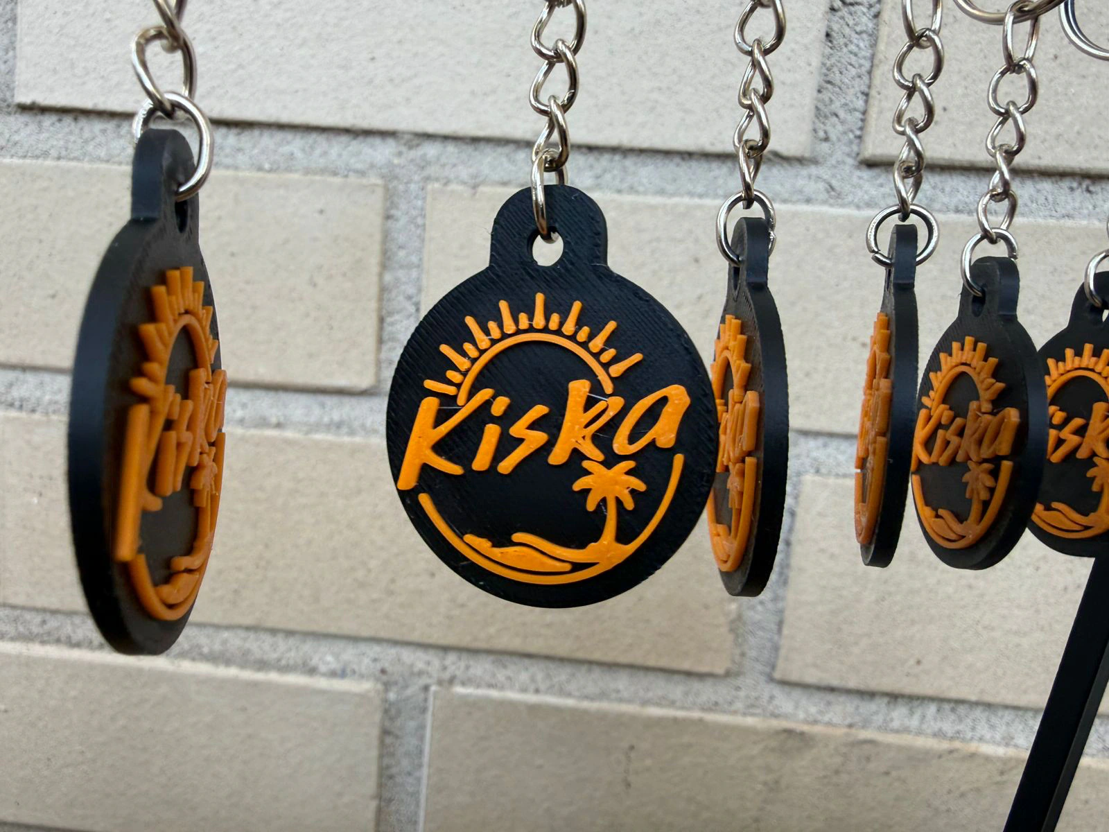 Black circular Kiska café keychains with bright orange raised logos on key rings.