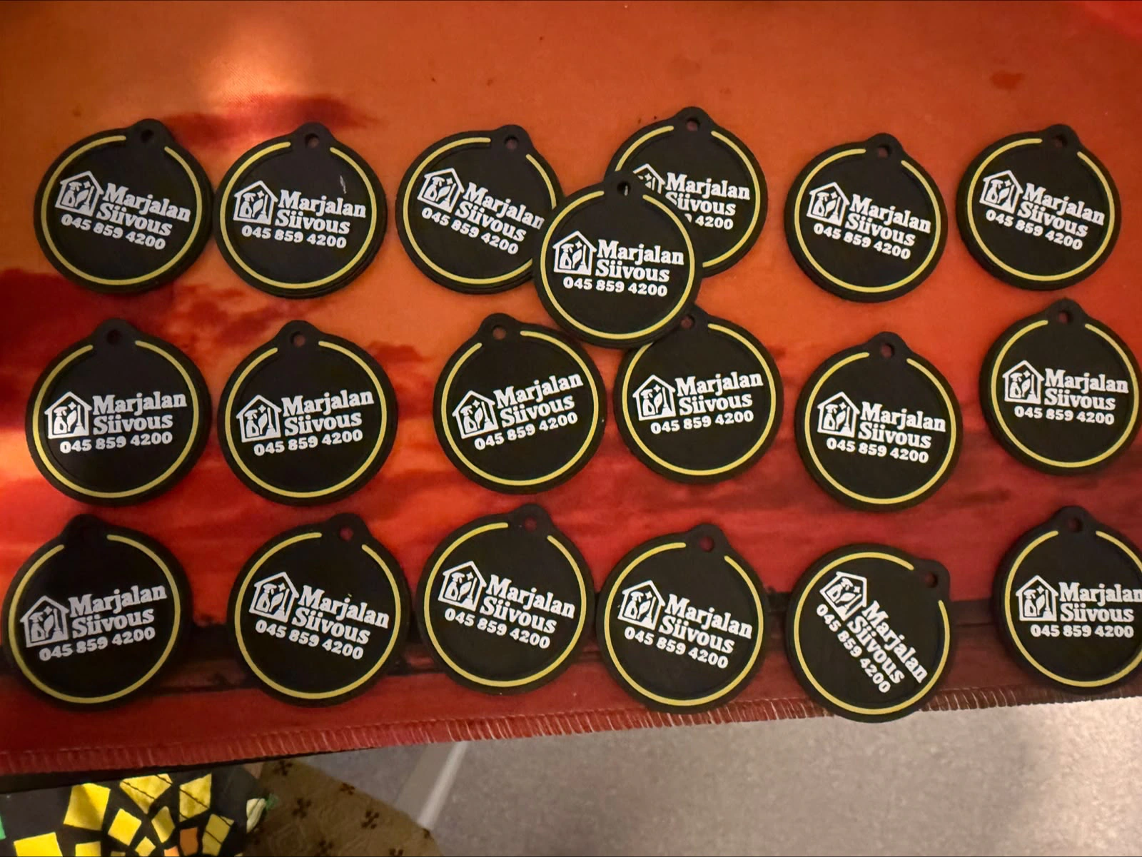 A batch of round black Marjalan Siivous branded keychains with white company lettering and yellow rings.